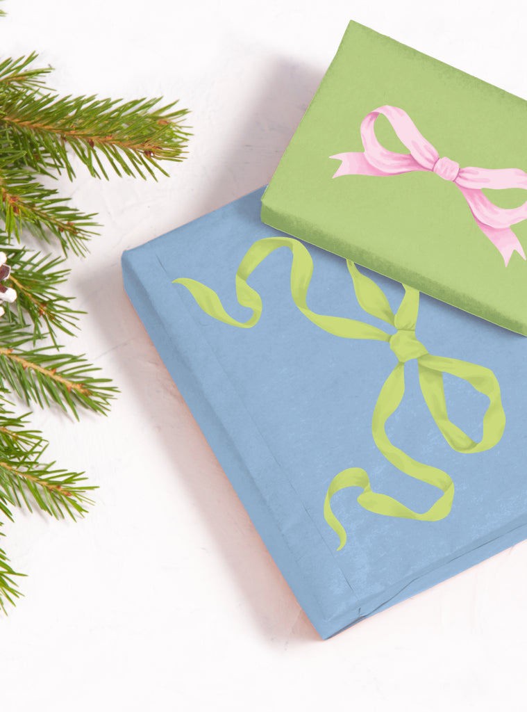 Two gift boxes decorated with pastel green and pink ribbon stickers beside holiday pine branches on white background
