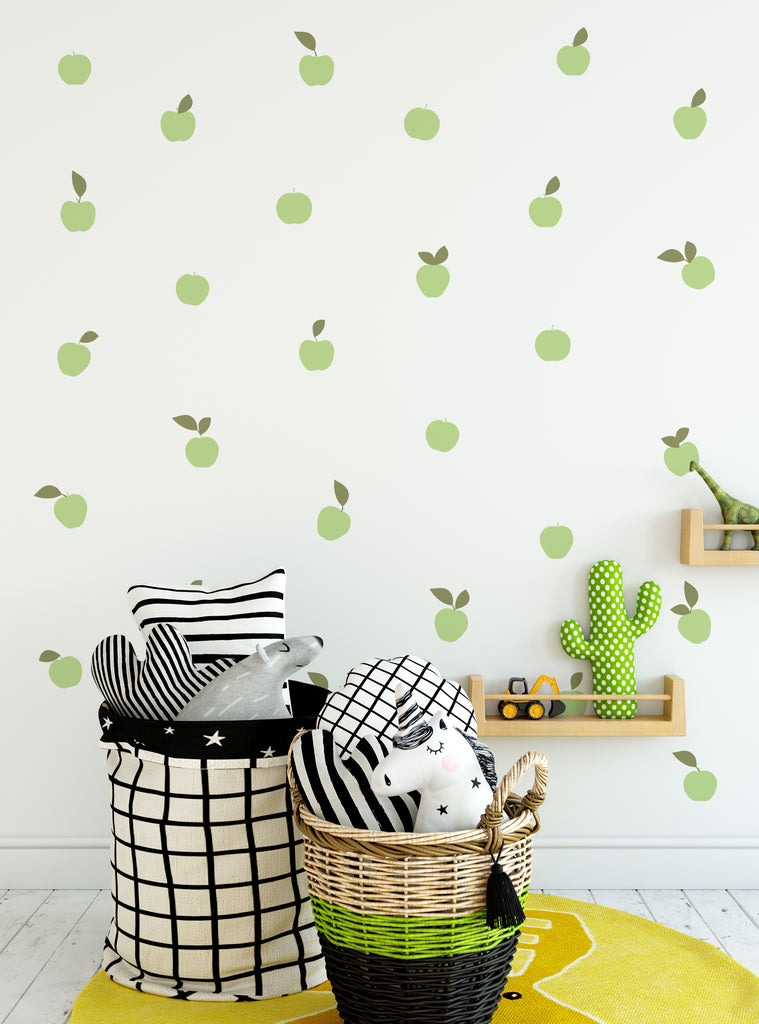 Green apple fruit wall decals scattered on a white wall above baskets and a shelf in a playful kids room setting