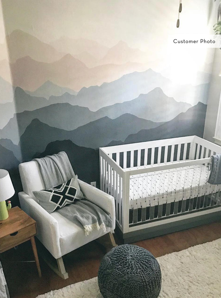 Cozy nursery featuring a mountain mural wallpaper with layered blue and grey tones creating depth and calm atmosphere.