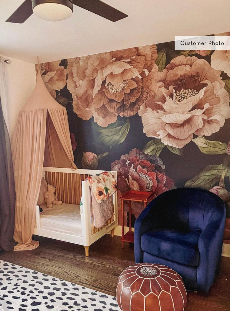 Cozy nursery with Bloom Flower Mural Wallpaper featuring large floral designs in soft beige and dark background, pink canopy, and navy chair.