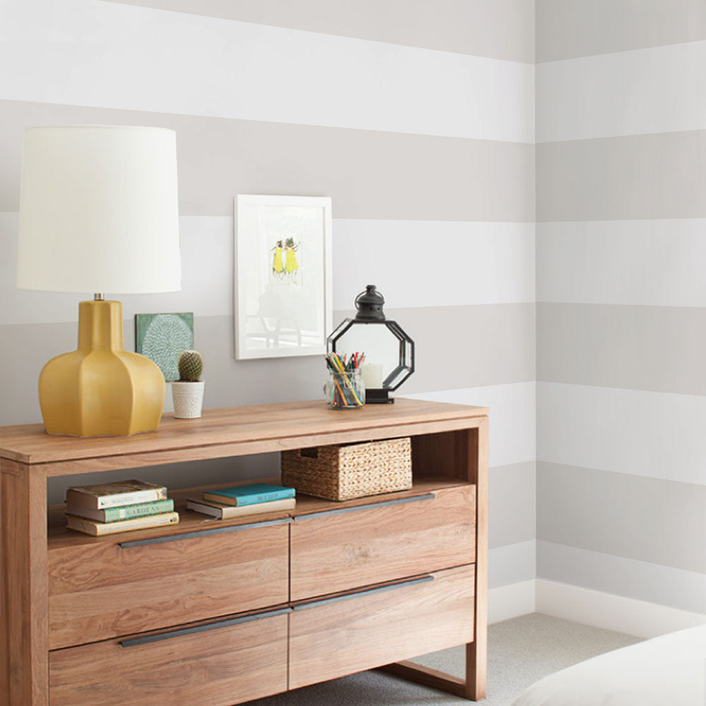 Calm bedroom corner with Horizontal Stripe Bold wallpaper in soft grey tones behind natural wood dresser and mixed decor pieces