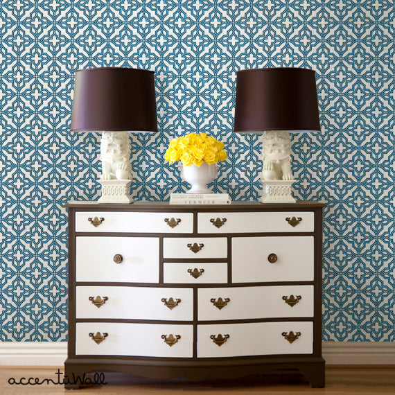 A stylish room featuring diamond flower wallpaper behind a classic wooden dresser with decorative lamps and yellow flowers on top