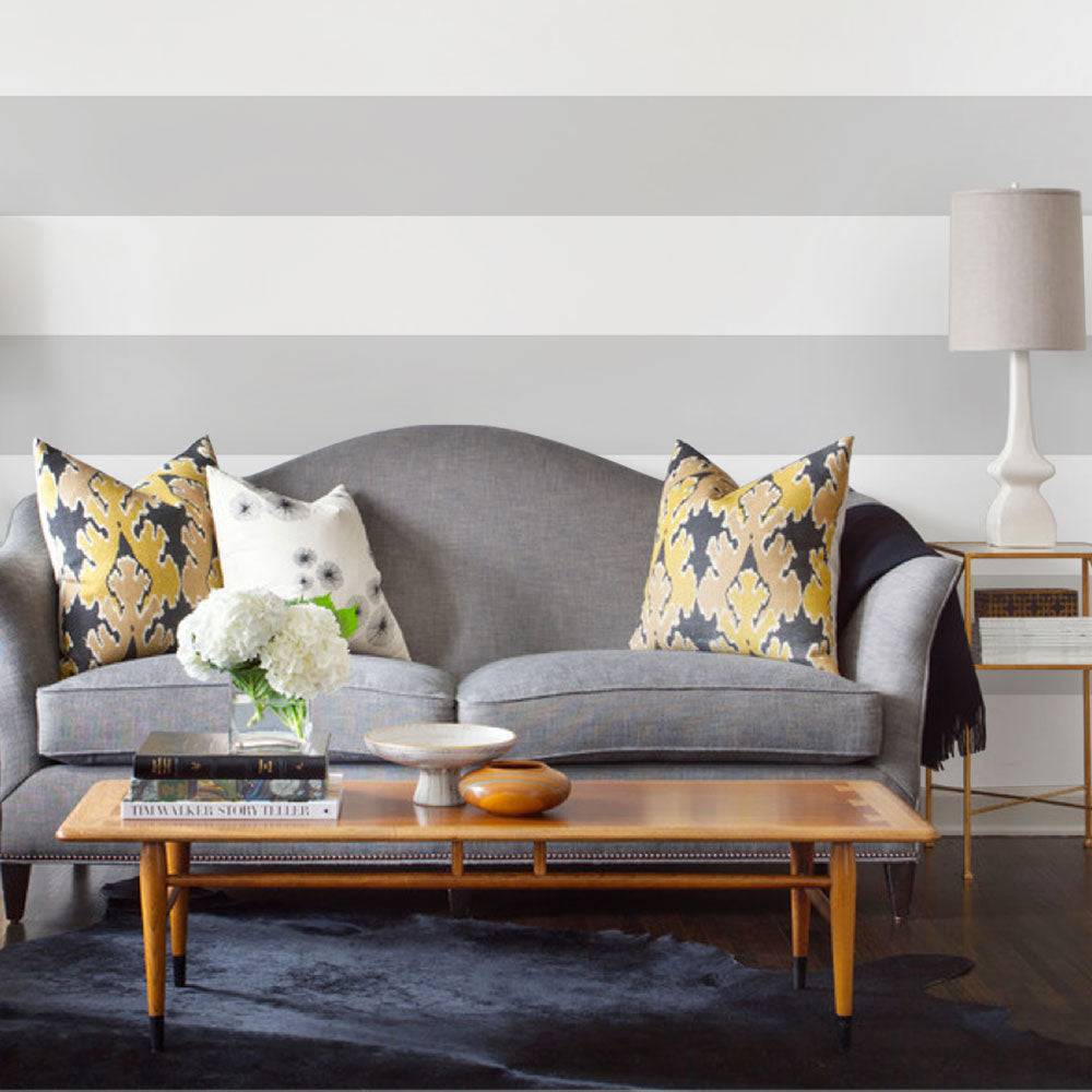 Living room scene with Horizontal Stripe Bold wallpaper in soft grey and white stripes behind a curved gray sofa and wooden coffee table setup