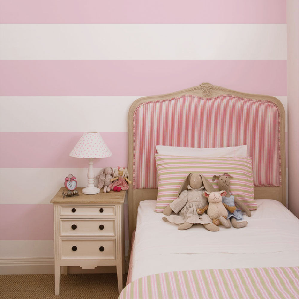 Kids and Baby Nursery Wallpaper featuring wide soft pink and white horizontal stripes with cozy bed and plush toys setting