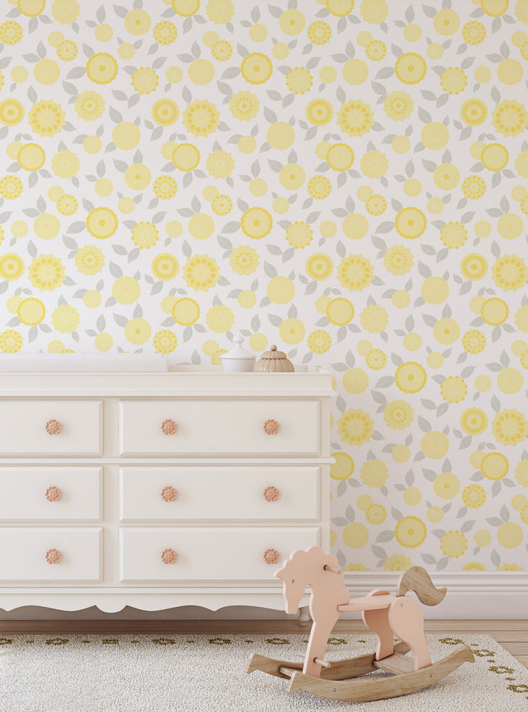 Bright modern flowers wallpaper with yellow blooms and grey leaves behind a white dresser and wooden rocking horse in nursery room