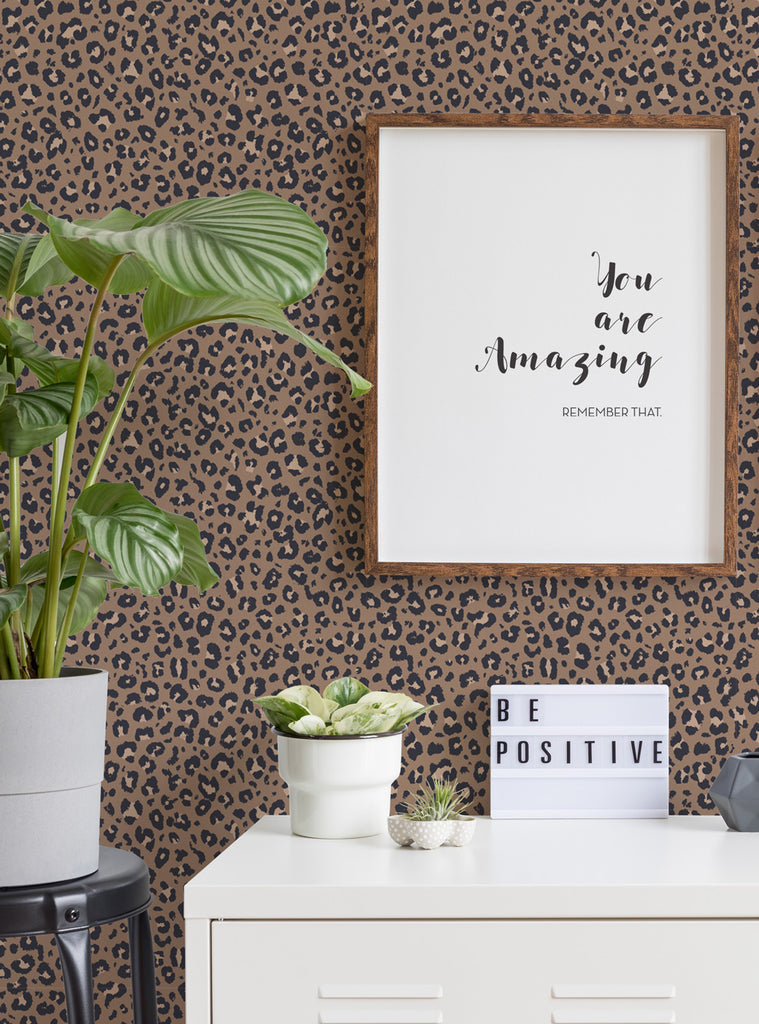 Leopard print wallpaper in brown tones adorning a room with green plants, positive message decor, and wooden framed typography art.
