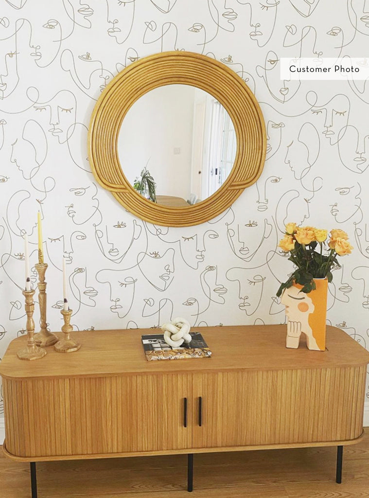 Modern entryway featuring minimalist faces line art wallpaper with a round wooden mirror and decorative accents on a wooden console table