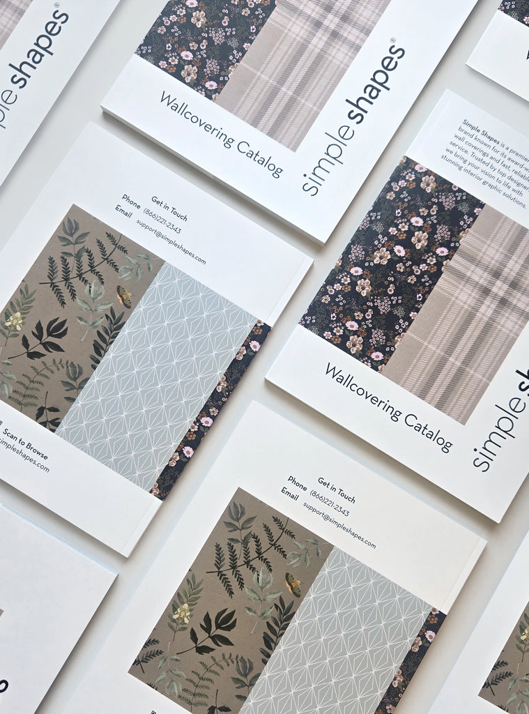 Multiple Simple Shapes wallcovering catalogs laid out showing floral, geometric, and plaid wallpaper designs in a casual flat lay style.