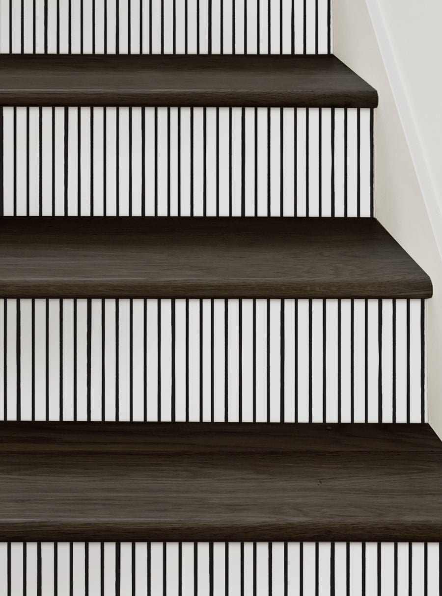 This image shows a set of wooden stairs with a unique hand-drawn painted vertical line pattern on the riser portion of the steps. The design creates a modern, artistic look that can add visual interest and character to any staircase. The peel and stick format allows for easy installation and repositioning, making it a versatile and convenient option for updating the stairs. This image would be an excellent representation of the Painted Vertical L