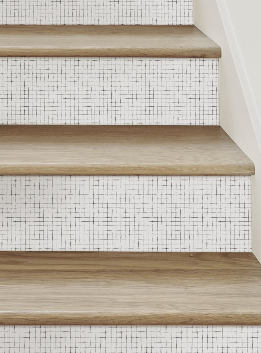 A geometric pattern of black and white tiles covers the stairs, creating a clean and modern look. The wooden stair treads provide a natural contrast to the tile design, adding warmth and texture to the space. This image showcases the Crosshatch Peel and Stick Stair Riser Strips, which can be easily applied to stairs for a unique and decorative touch. These durable, repositionable vinyl stickers are a versatile and convenient way to update the loo