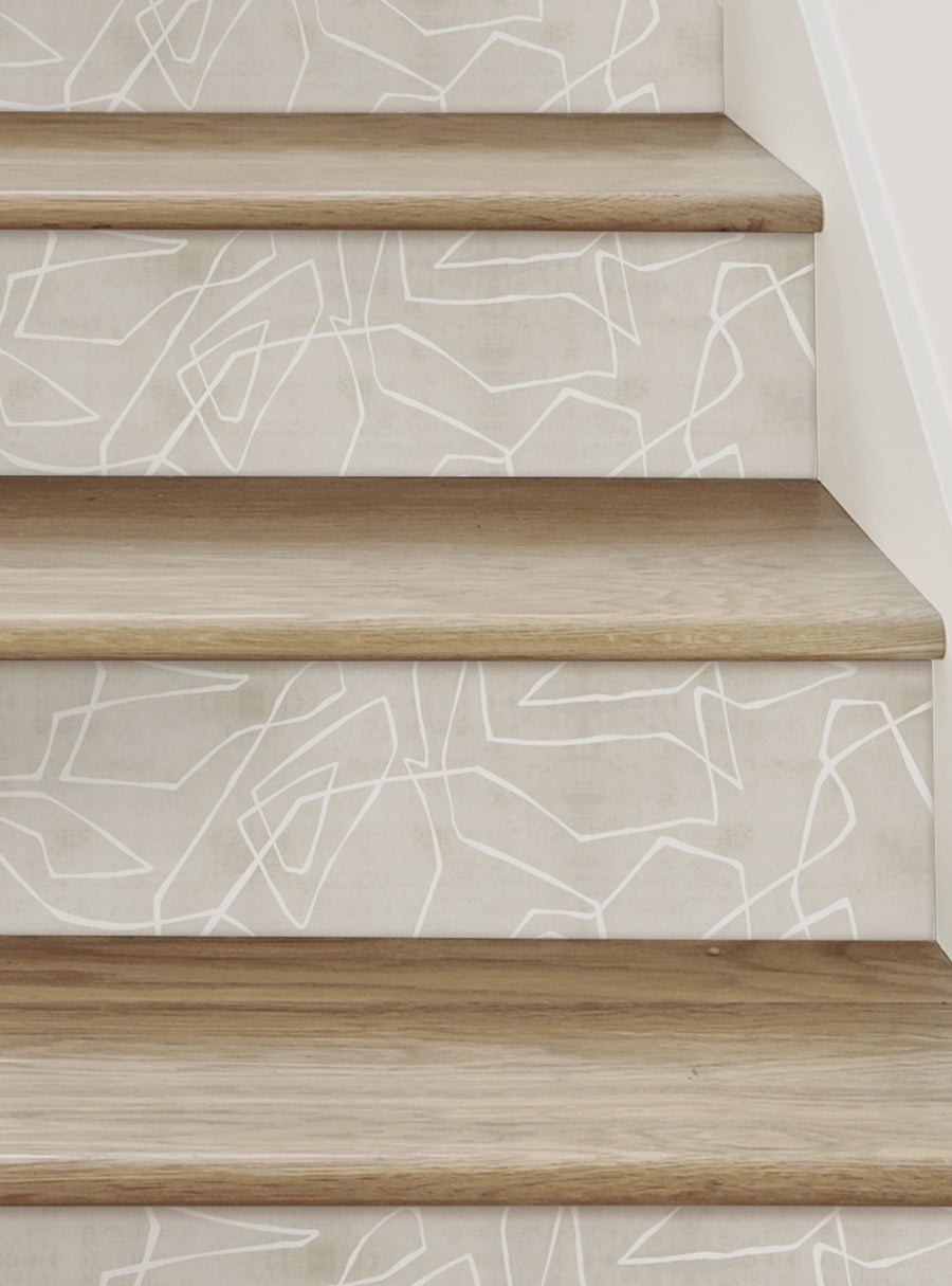 The image shows a set of wooden stairs with a textured, geometric pattern on the riser strips. The pattern features an entangled lines design that creates a contemporary and luxurious look, adding a beautiful accent to the stairs. The pattern is printed on a premium adhesive vinyl that can be easily applied and repositioned, providing a mess-free and stress-free installation experience. Featured Collection, Top Sellers, Stair Riser Decals, All Pr