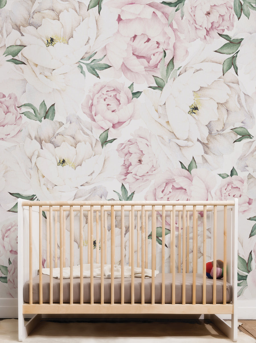 A serene nursery featuring a floral wallpaper with soft pink and white peonies. In the foreground, there is a modern wooden crib with a light beige mattress. A small blanket is draped over the side of the crib, and a colorful soft toy is resting inside. The floral design on the wall adds a gentle and calming atmosphere to the space.