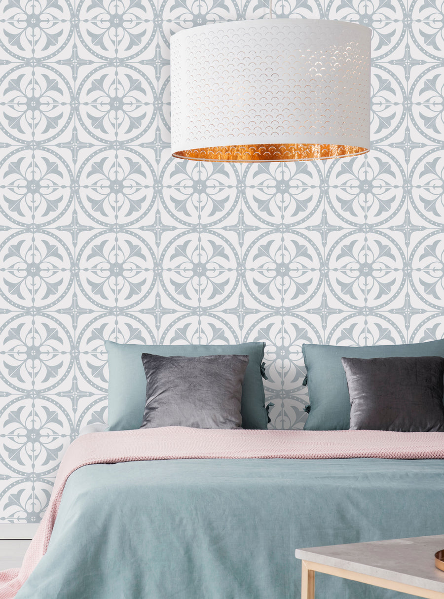 The image depicts a bedroom with a patterned wallpaper featuring a repeating geometric design. The wallpaper has a subtle gray and white color scheme, creating a calming and sophisticated look. The room is furnished with a bed, bedside tables, and pillows in muted tones, complementing the wallpaper's aesthetic. This Round Moroccan Tile Wallpaper would be an ideal choice for adding a touch of elegance and style to any room in the home. , Top Selle