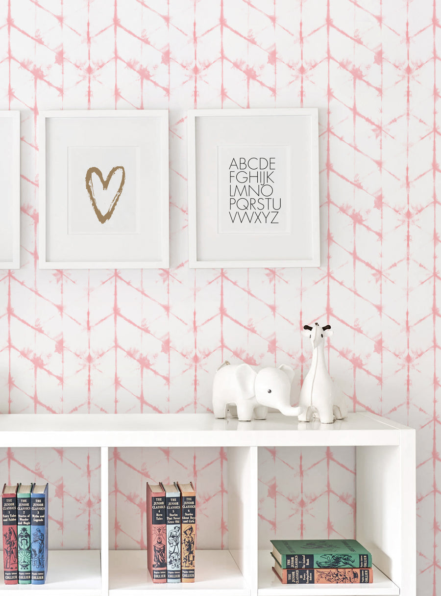 An abstract hexagon pattern in soft pink and white tones covers the wallpaper, creating a stylish and modern backdrop for this cozy nursery setting. The white frames showcase minimalist wall art featuring a heart design and the alphabet, adding a touch of whimsy and personalization. The curated shelving displays various children's books and decorative elements, creating a visually appealing and inviting space. , Top Sellers,Peel and Stick Wallpap