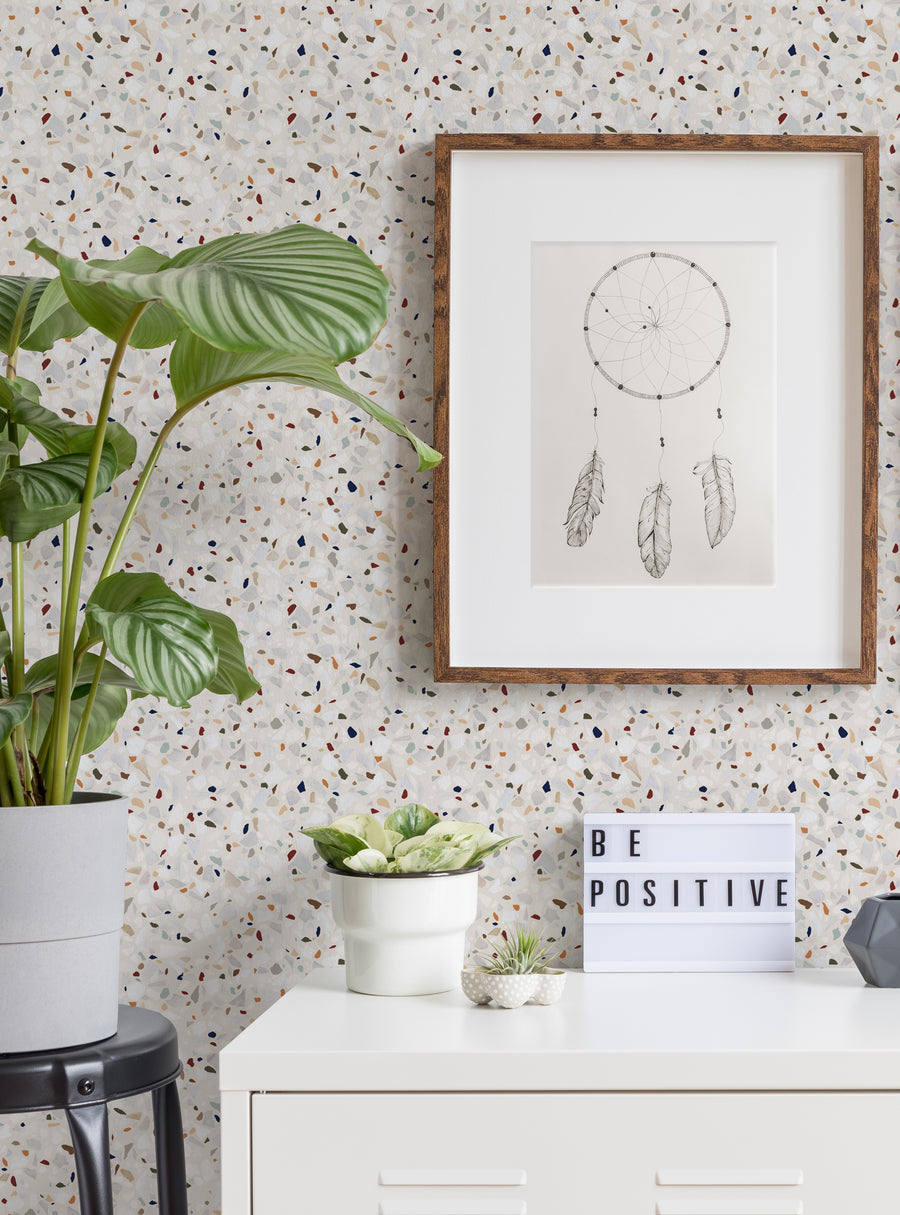 Decorative terrazzo wallpaper with a repeating pattern of abstract stone-like shapes in various neutral tones, providing a visually interesting backdrop for the framed dreamcatcher artwork and potted plants in the room. , Top Sellers, Peel and Stick Wallpaper, Surface & Texture Wallpaper, Geometric & Pattern Wallpaper, Kids and Baby Nursery Wallpaper, Abstract Murals and Wallpaper, All Products, Unpasted Wallpaper, Wallpaper and Murals